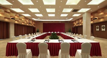 Un salón de conferencias con una larga mesa, sillas blancas y una alfombra roja.