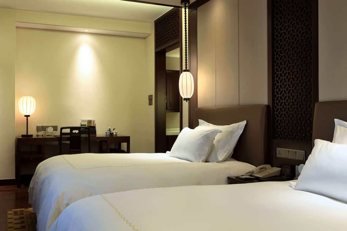 A hotel room with two beds, a desk with a lamp, and a telephone.