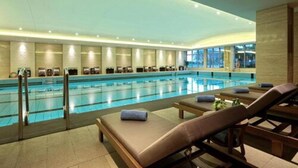 A large indoor swimming pool with multiple lanes, surrounded by lounge chairs and a glass wall. - Hangzhou Tianyuan Tower Hotel (Hangzhou)