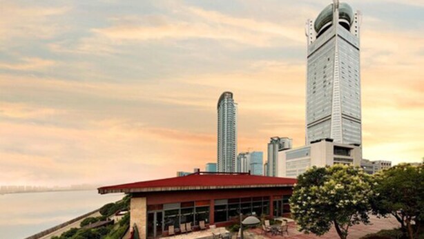 A modern building with a red roof and a glass facade, surrounded by greenery and a waterfront view. - Hangzhou Tianyuan Tower Hotel (Hangzhou)