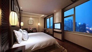A hotel room with a large bed, a desk, a chair, a TV, and a view of the city at dusk. - Hangzhou Tianyuan Tower Hotel (Hangzhou)