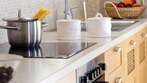 A kitchen with wooden cabinets, a stainless steel sink, and a fruit basket on the counter. - Violitzis Villas (Lefkada)
