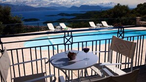 A poolside area with a table, chairs, and a glass of red wine. - Violitzis Villas (Lefkada)