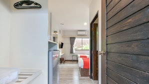 A narrow hallway with a kitchen area on the left, a bed with a red blanket in the center, and a wooden door on the right. - OYO 145 Pattaya Bed Boutique (Pattaya)