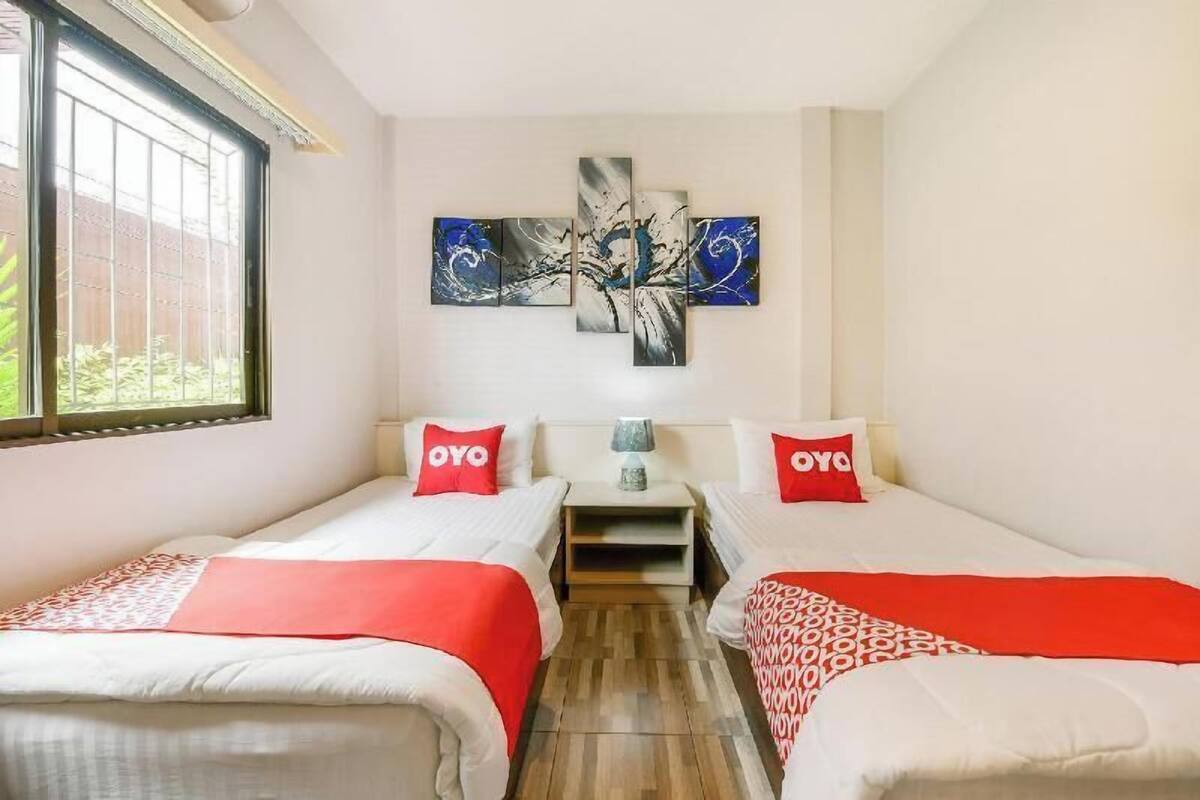 Une chambre d’hôtel avec deux lits, une fenêtre, une œuvre d’art accrochée au mur et une petite table avec une lampe.
