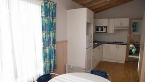 A compact kitchen with white cabinets, a microwave, and a dining area with a round table and two chairs. - Tuross Lakeside Tourist Park (Tuross Head)