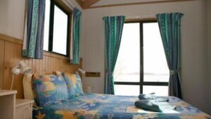 A bedroom with a bed, curtains, a window, and a bedside lamp. - Tuross Lakeside Tourist Park (Tuross Head)