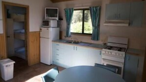 A compact kitchen with a microwave, stove, and cabinets. - Tuross Lakeside Tourist Park (Tuross Head)