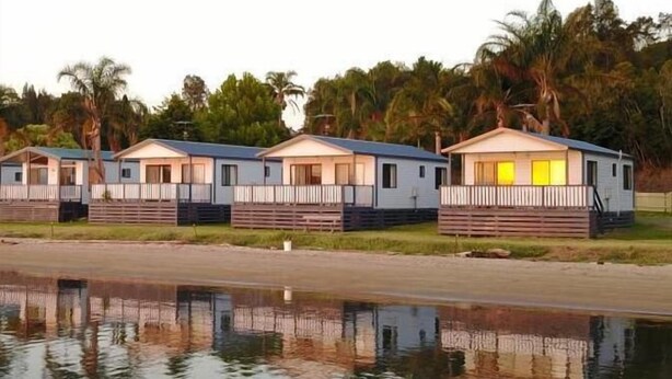 A row of mobile homes with a reflective water body in the foreground. - Tuross Lakeside Tourist Park (Tuross Head)
