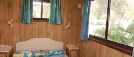 A bedroom with wooden walls, a bed with a colorful bedspread, two bedside tables, and a window with curtains.