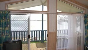 A room with a sliding glass door leading to a balcony with a wooden deck and a metal fence. - Tuross Lakeside Tourist Park (Tuross Head)
