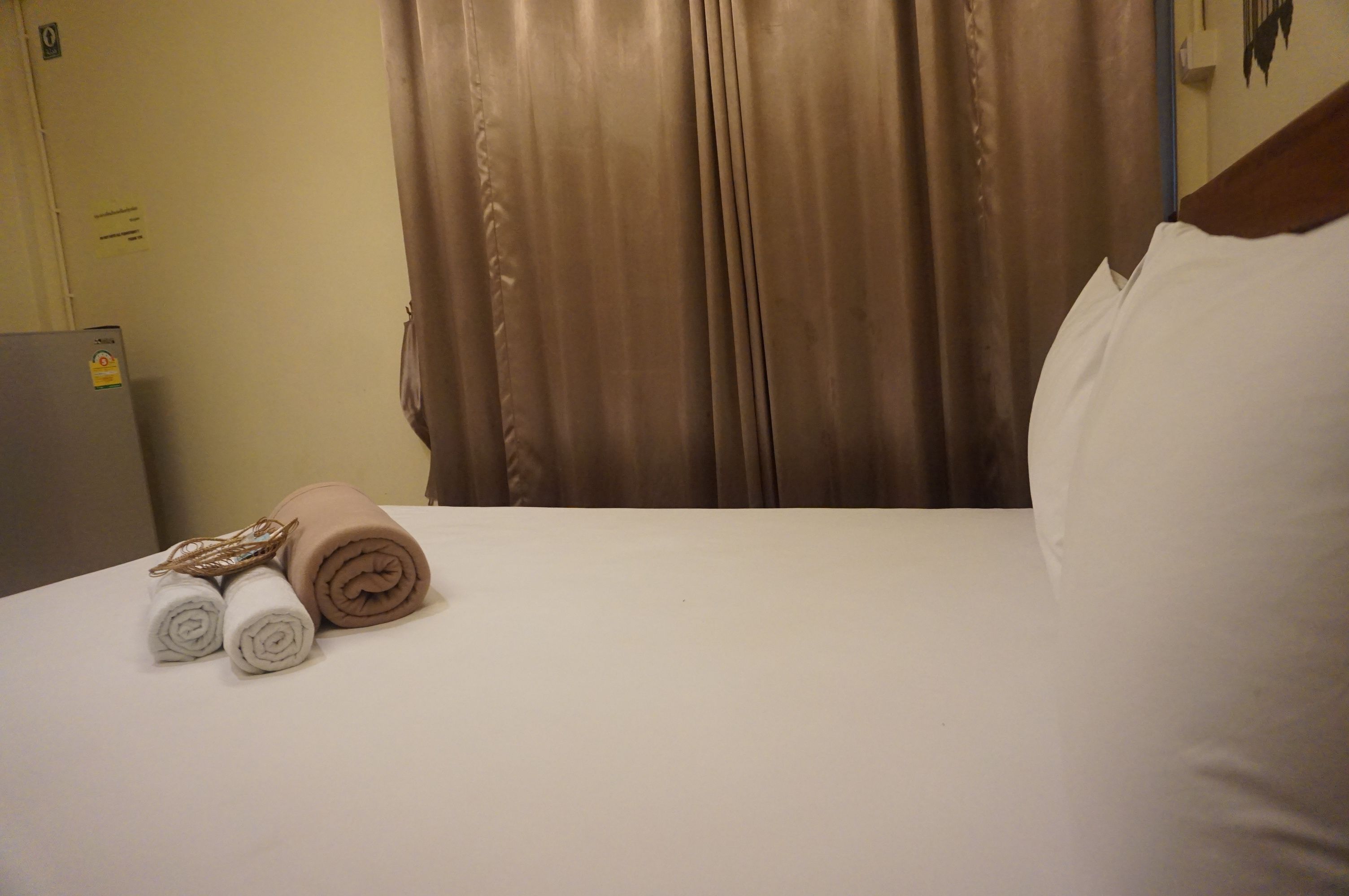 Una habitación de hotel con una cama, dos toallas enrolladas y una cortina.