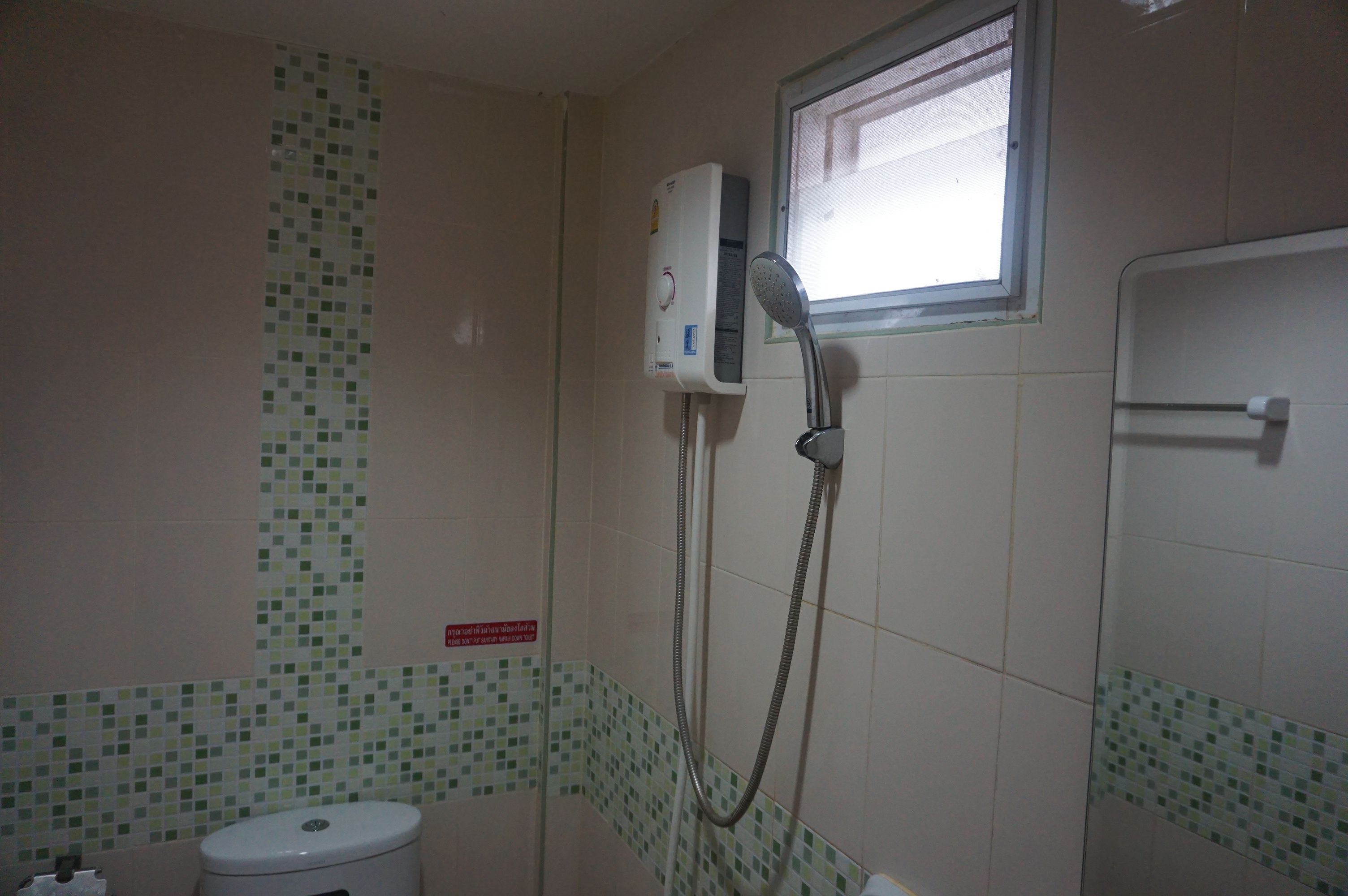Un baño con inodoro, ducha con cabezal de ducha manual y ventana.