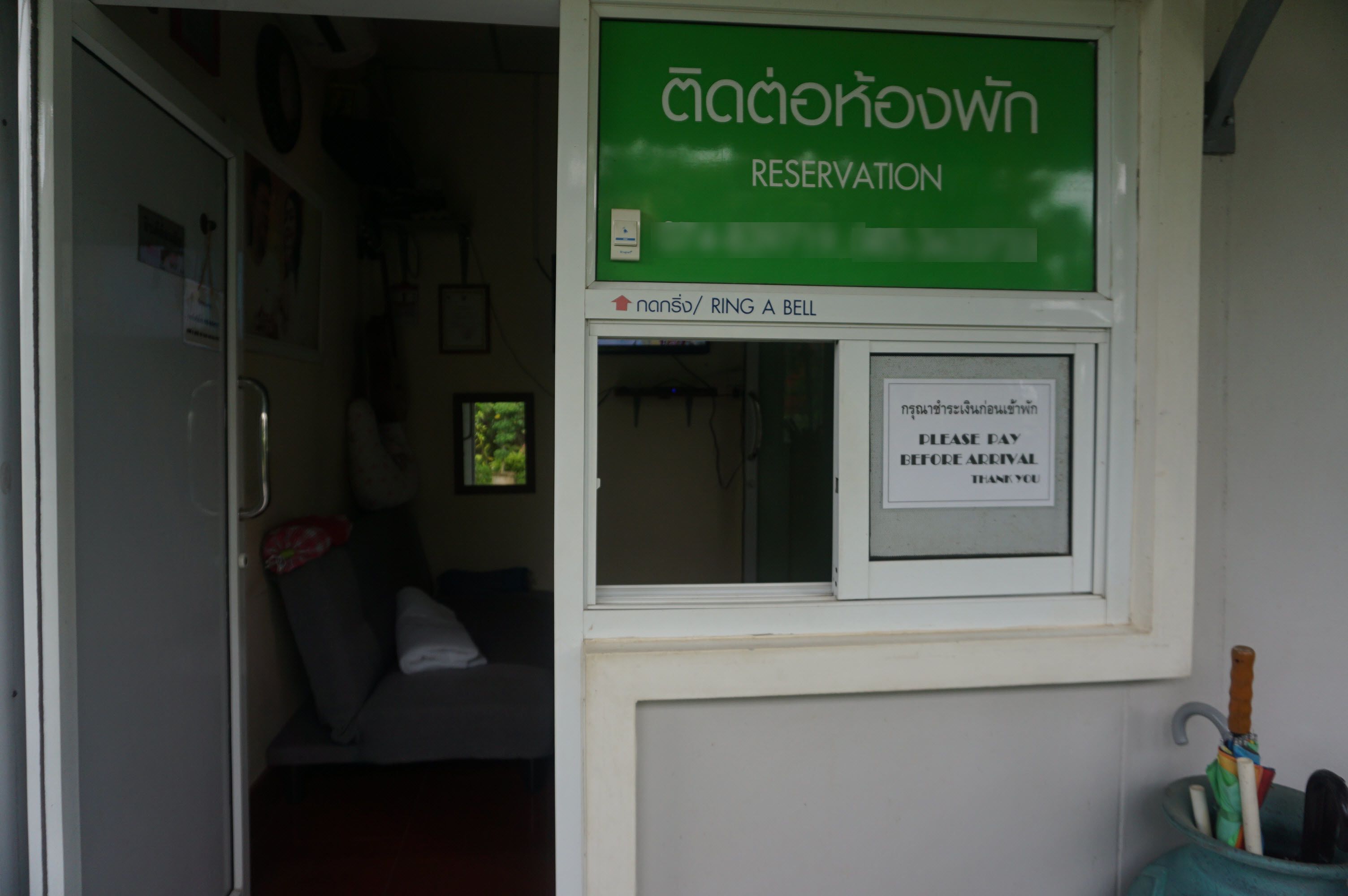 A room with a green sign indicating a reservation desk, a bell for assistance, and a sign requesting payment before arrival.
