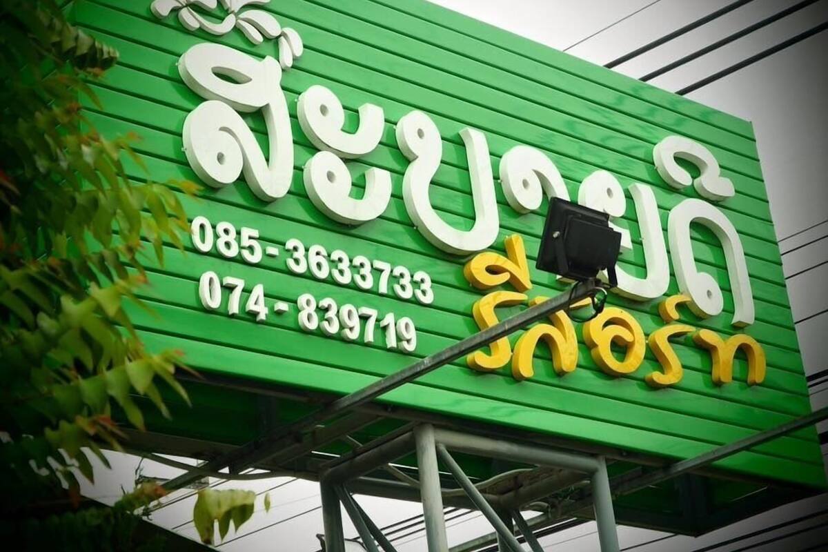 Un cartel verde con texto blanco y amarillo, posiblemente el nombre de un negocio o un anuncio, y dos números de teléfono.