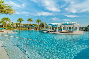 A large outdoor swimming pool with lounge chairs and umbrellas, surrounded by palm trees and a clear sky. - Windsor At Westside #14 - 9 Bed 6 Baths Villa (Kissimmee)