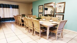 A dining area with a long wooden table and matching chairs, a clock on the wall, and framed artwork above the table.