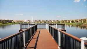 A wooden deck leading to a body of water with a view of houses in the background.