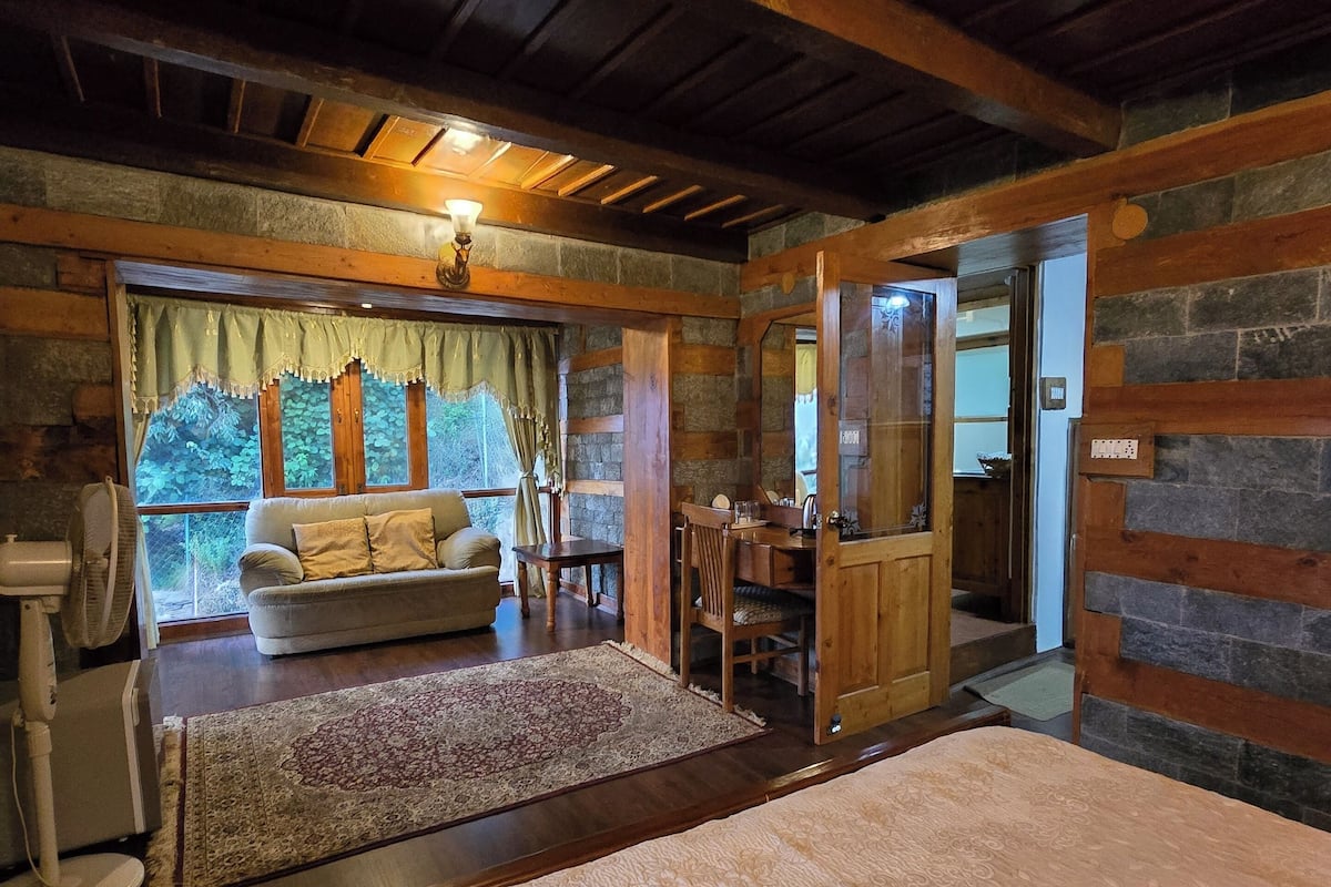A cozy room with a bed, a sofa, a dining table, and a stone wall.