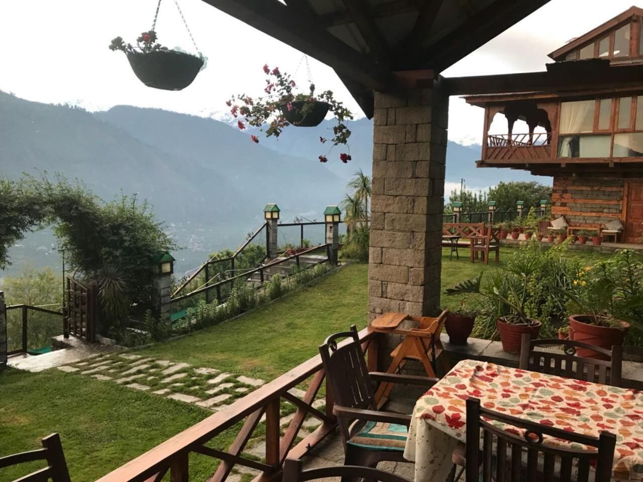 Una terraza con mesa y sillas, un cesto de flores colgante y vistas a montañas.