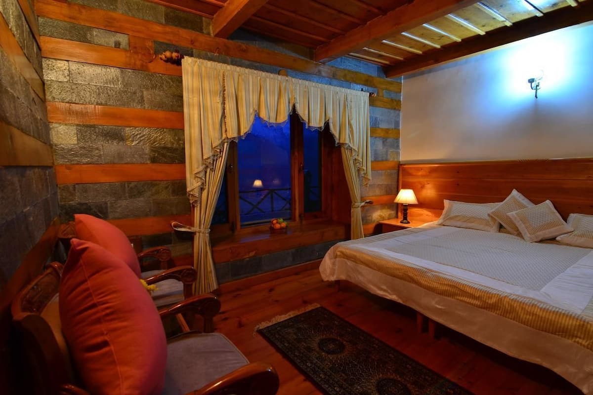A cozy room with a bed, a chair, a nightstand with a lamp, and a window with curtains.