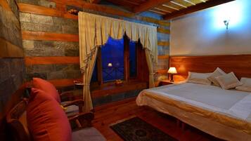A cozy room with a bed, a chair, a nightstand with a lamp, and a window with curtains.