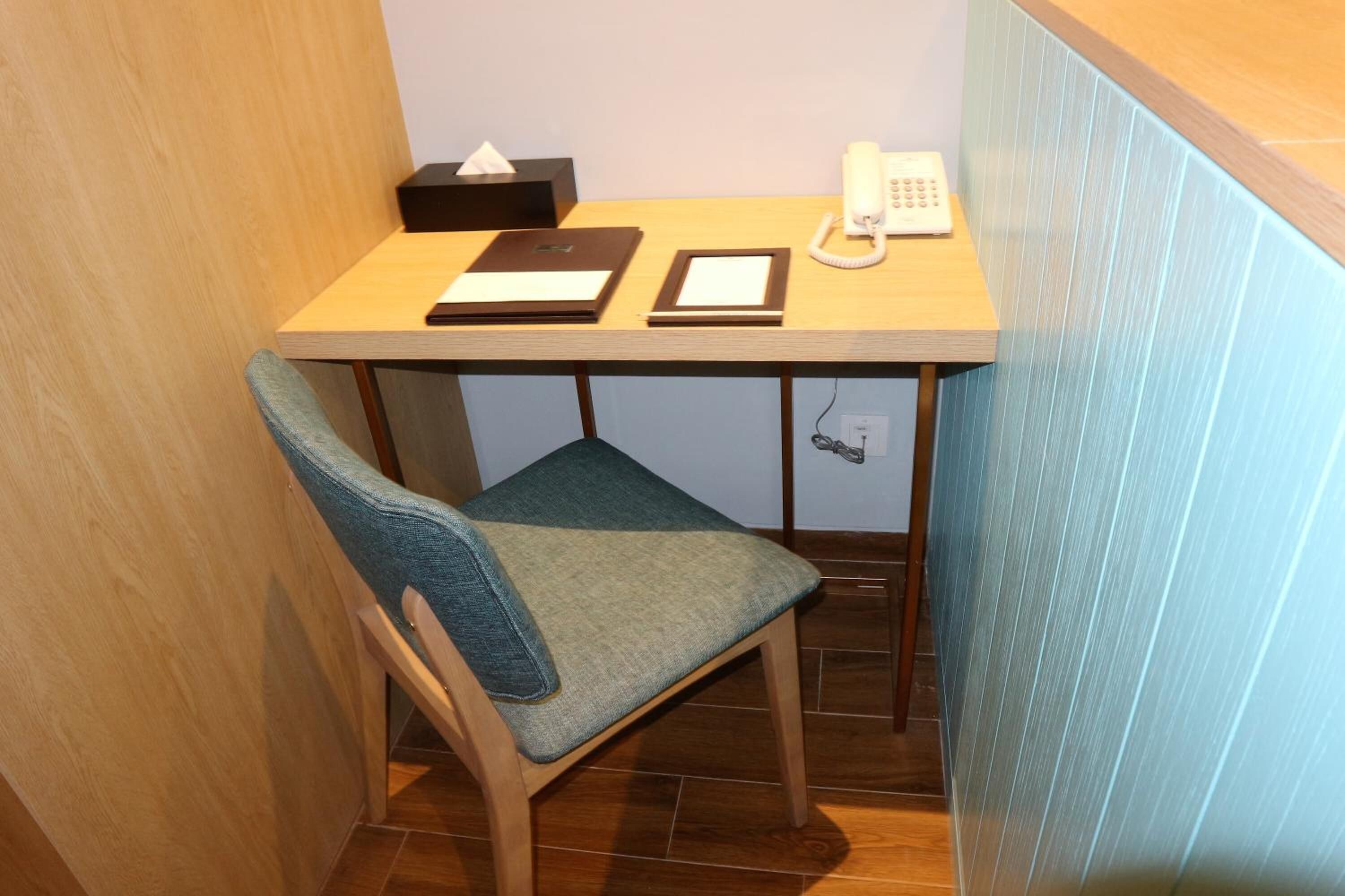 Un petit bureau en bois, une chaise, un téléphone, une boîte de mouchoirs et un classeur.