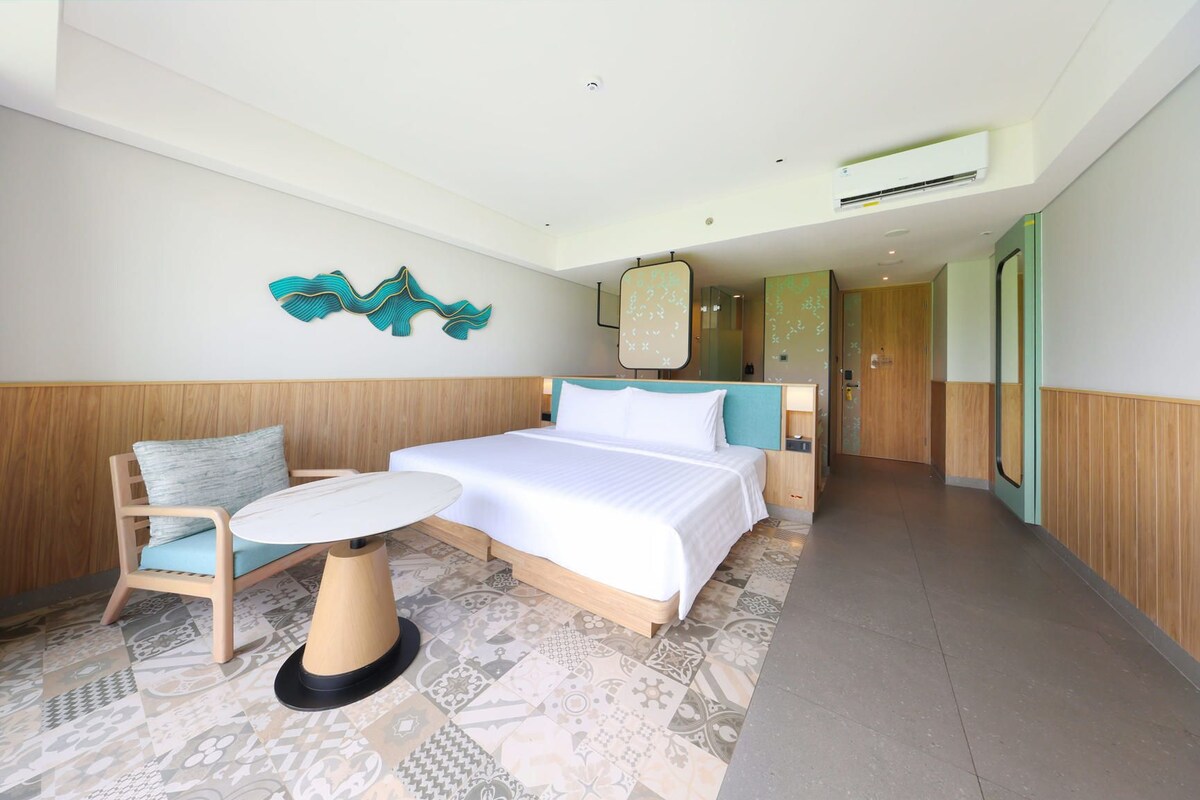 Una habitación de hotel con cama, una mesita, una silla y un adorno en la pared.