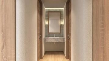 Un pasillo estrecho con suelo de madera y paredes, que conduce a un baño con lavamanos de mármol y un espejo encima.