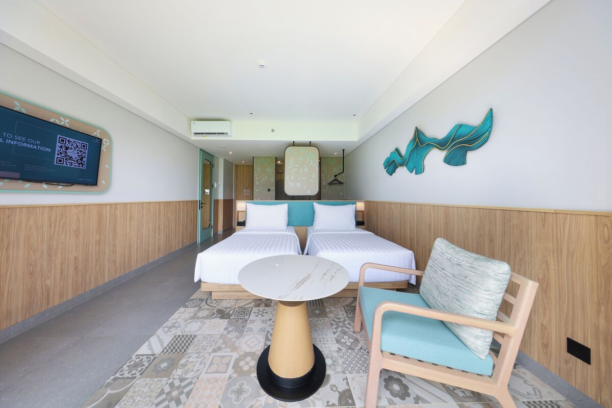 A hotel room with two beds, a round table, and a chair.