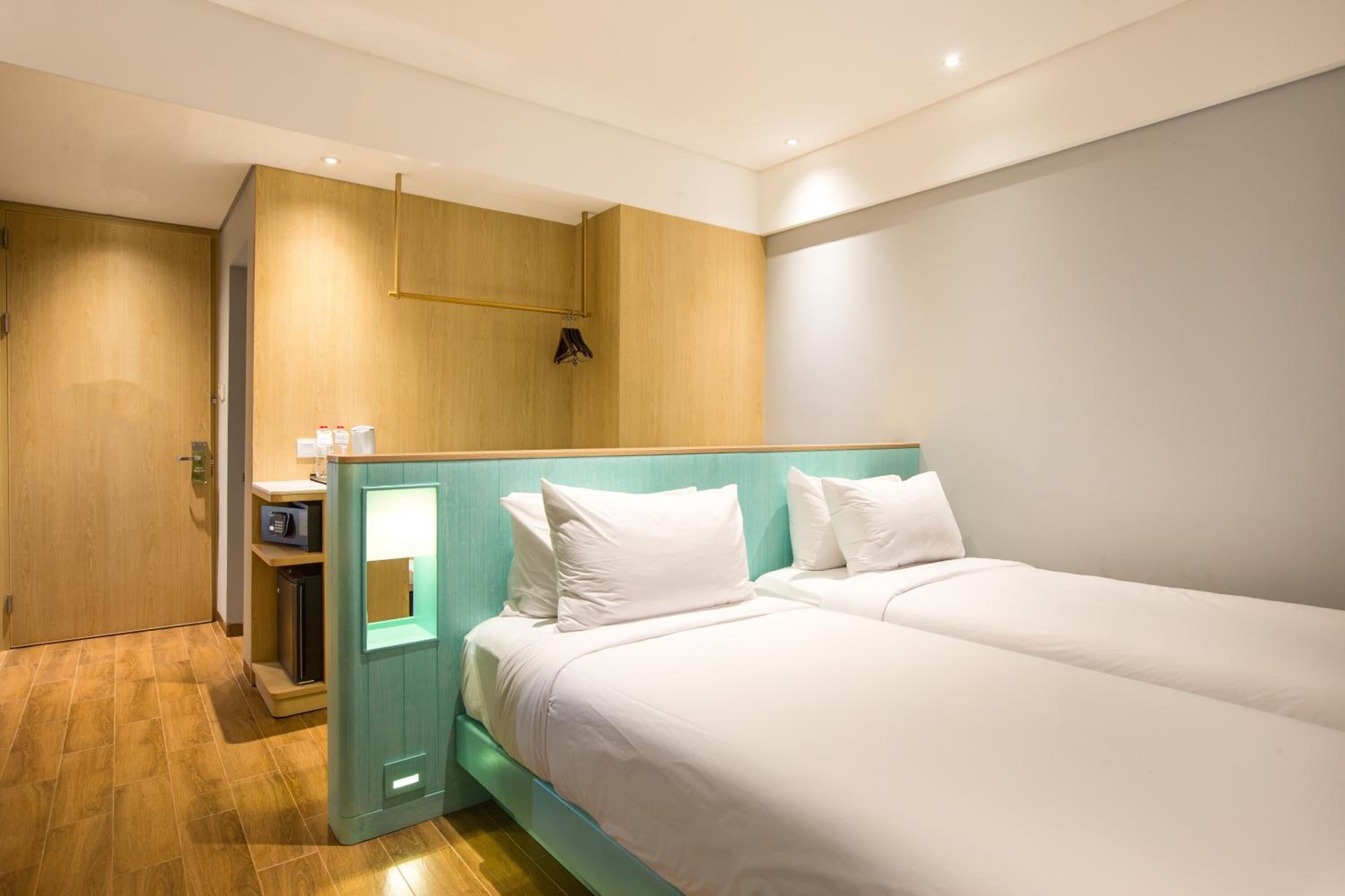 Habitación de hotel con dos camas, un armario de madera, un escritorio pequeño con lámpara y un microondas.