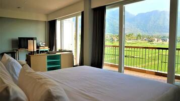A hotel room with a large bed, a desk with a TV, and a balcony with a mountain view.