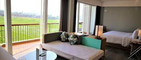 A hotel room with a balcony, a sofa, a bed, and a small table.