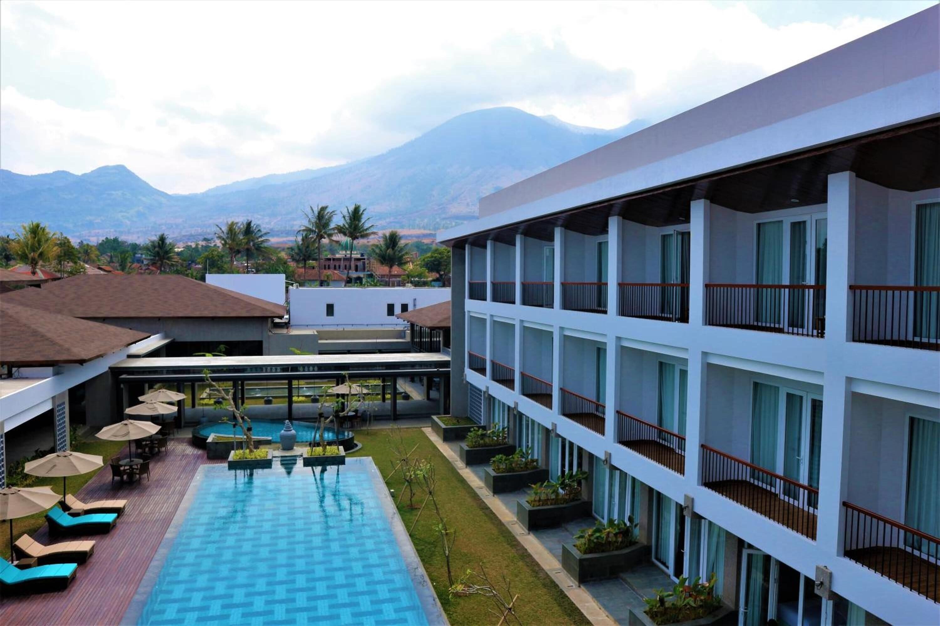 A hotel with a swimming pool, outdoor seating, and a view of mountains.