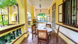 A covered outdoor dining area with a pool in the background, surrounded by yellow walls and tropical plants. - Casugria Dutch Heritage Residence (Malacca City)