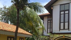 A two-story building with a tiled roof, a swimming pool, and a well-maintained garden with palm trees and other plants. - Casugria Dutch Heritage Residence (Malacca City)