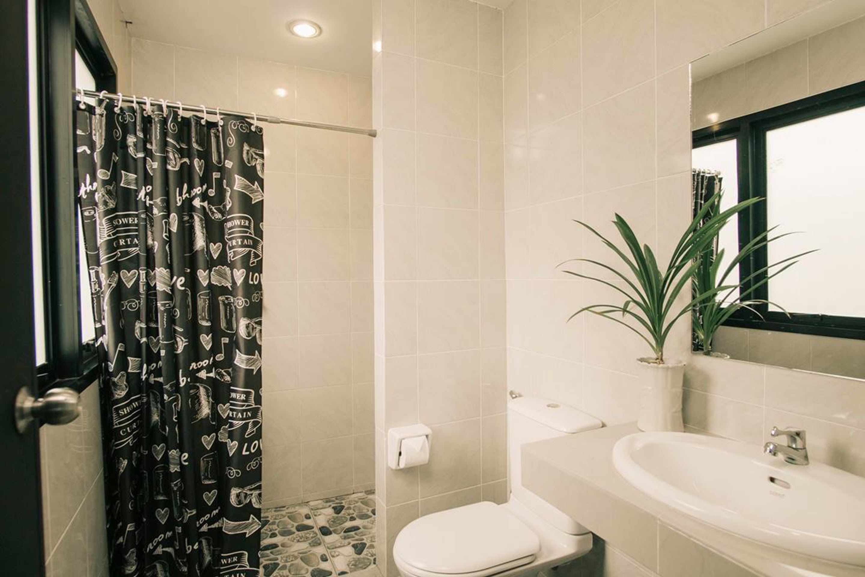 A bathroom with a shower curtain featuring musical notes and hearts, a toilet, a sink, and a potted plant.