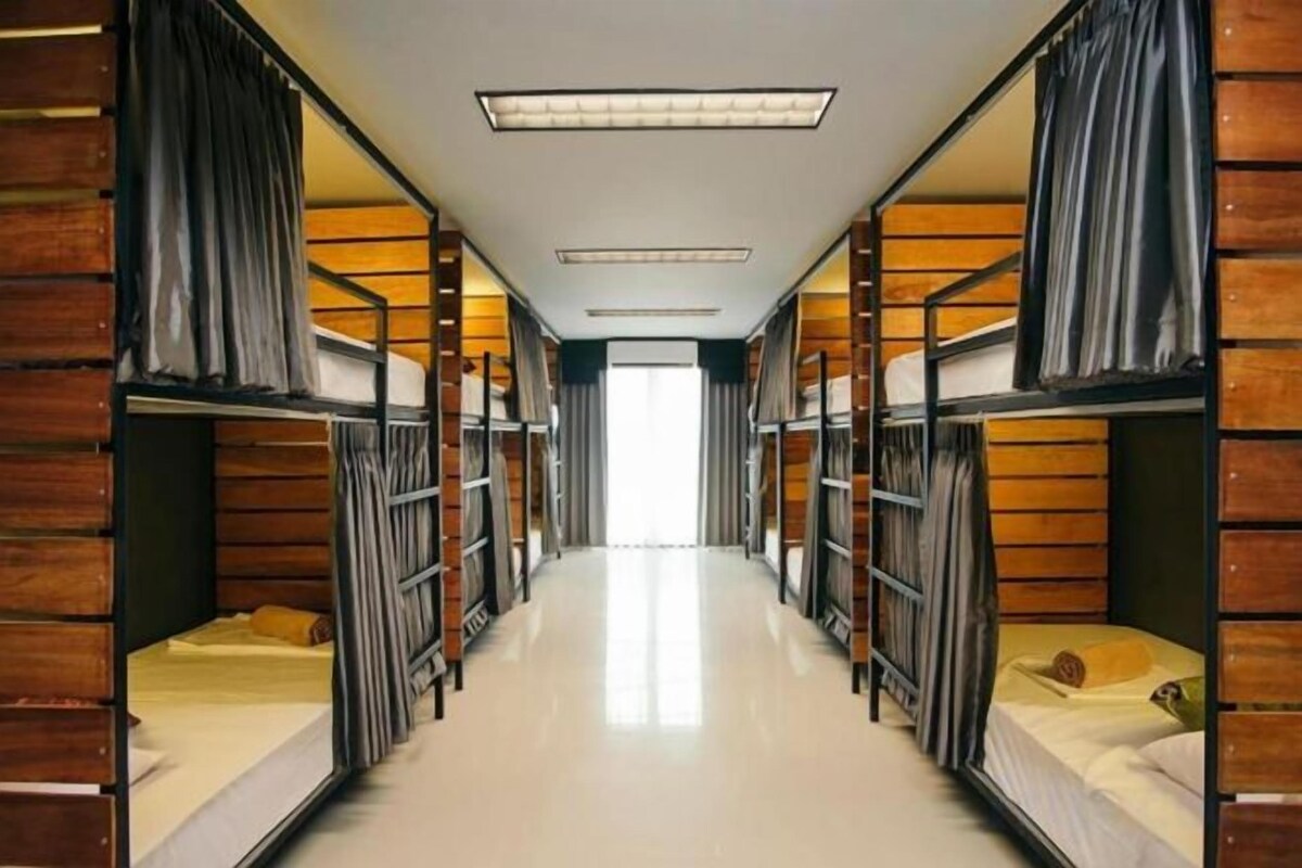 A corridor with bunk beds on either side, a ceiling light, and a view into the distance.