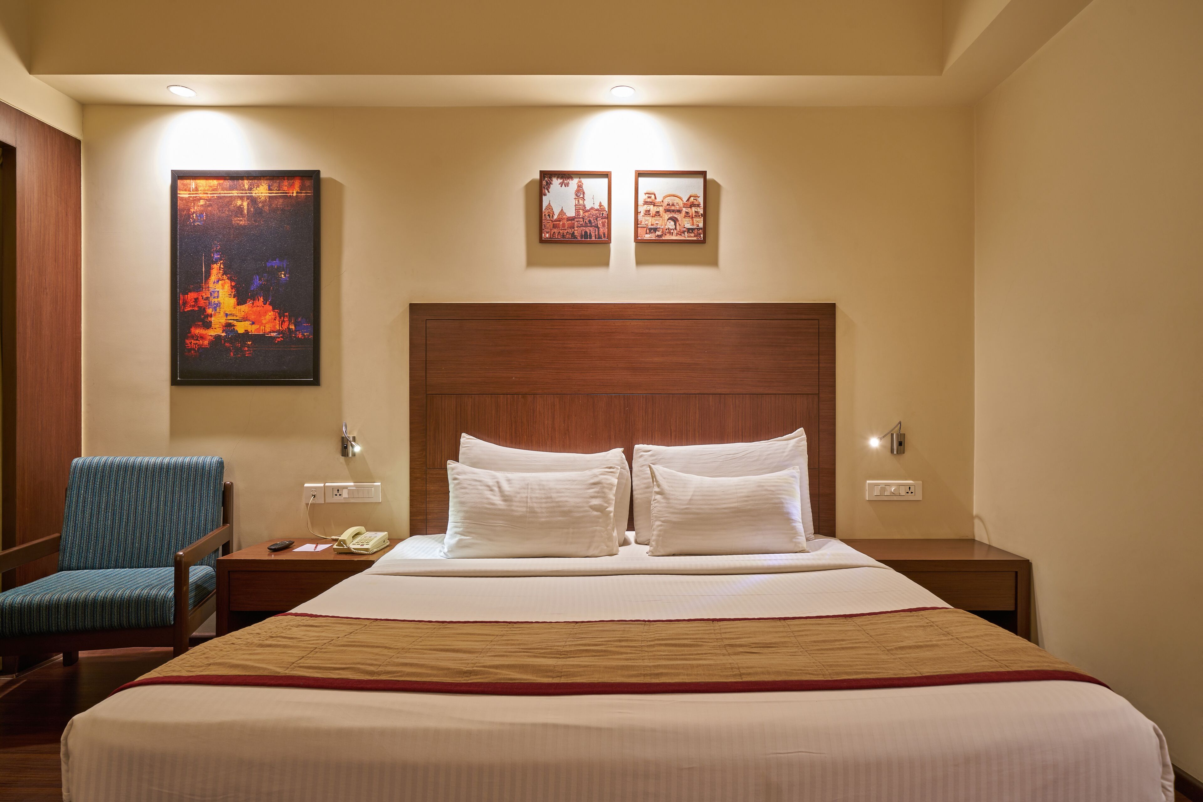 A hotel room with a large bed, a chair, a nightstand, and a wall-mounted phone.