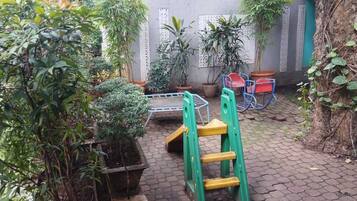 Un patio con plantas en macetas, una escalera verde y sillas rojas.