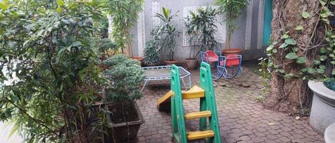 A courtyard with potted plants, a green ladder, and red chairs.