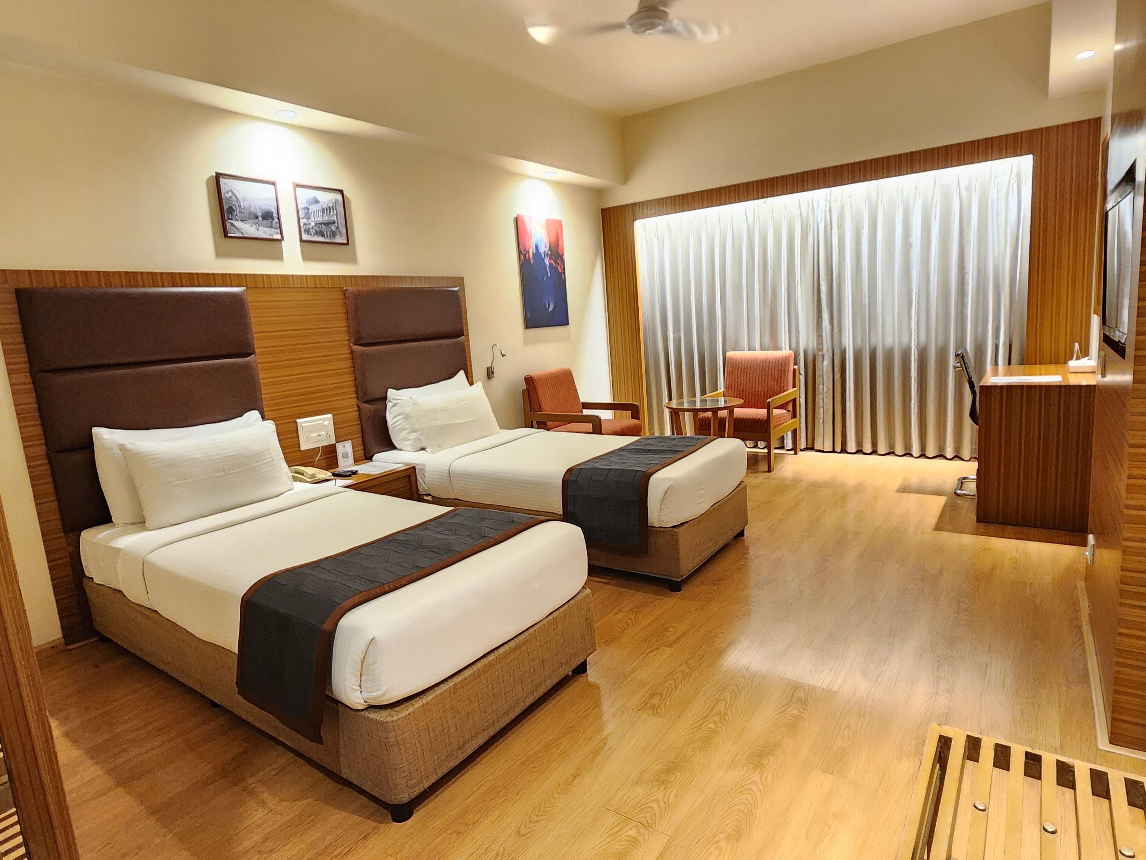 A hotel room with two beds, a desk, a chair, and a large window with curtains.