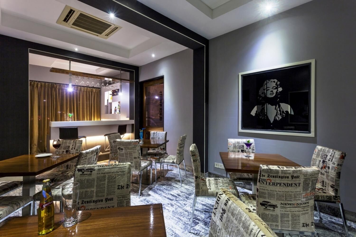 A modern dining area with newspaper-patterned chairs, a wooden table, and a framed artwork on the wall.