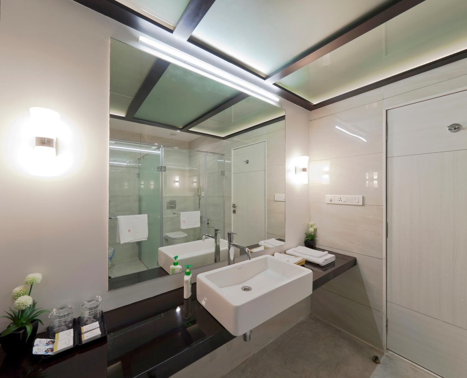 A modern bathroom with a large mirror, two sinks, and a glass-enclosed shower.