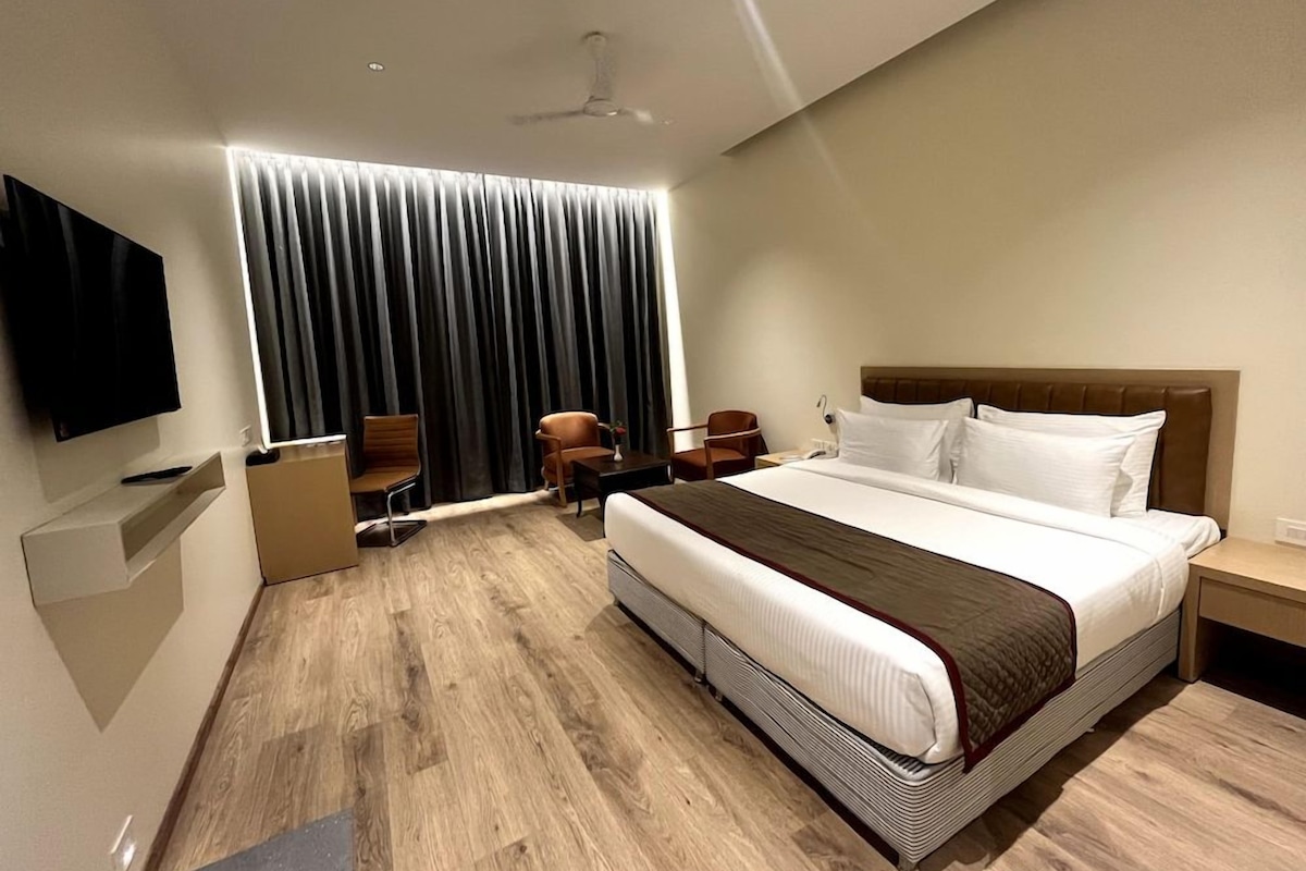 Quarto de hotel moderno com uma cama grande, televisão de tela plana na parede, escrivaninha com cadeira e janela com cortinas.