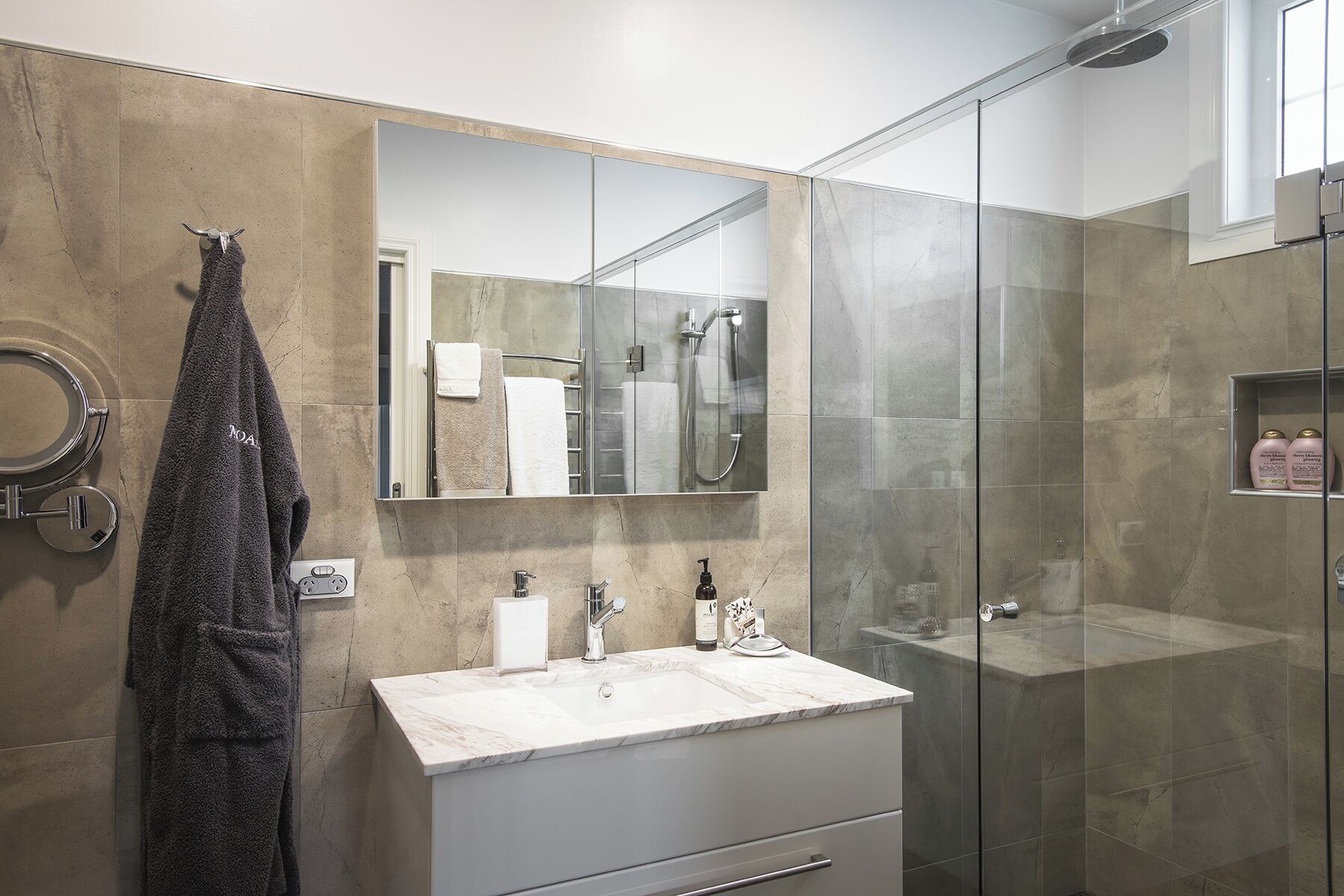 Een moderne badkamer met een douchecabine van glas, een marmeren wastafel en een handdoekhouder.