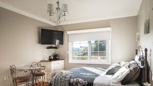 Quarto com cama, televisão, janela e uma pequena mesa com cadeiras.