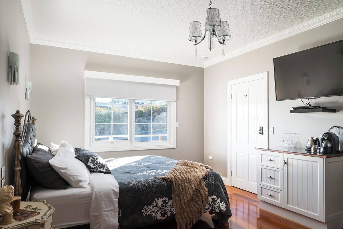 A bedroom with a bed, a window, a TV, and a kitchenette.