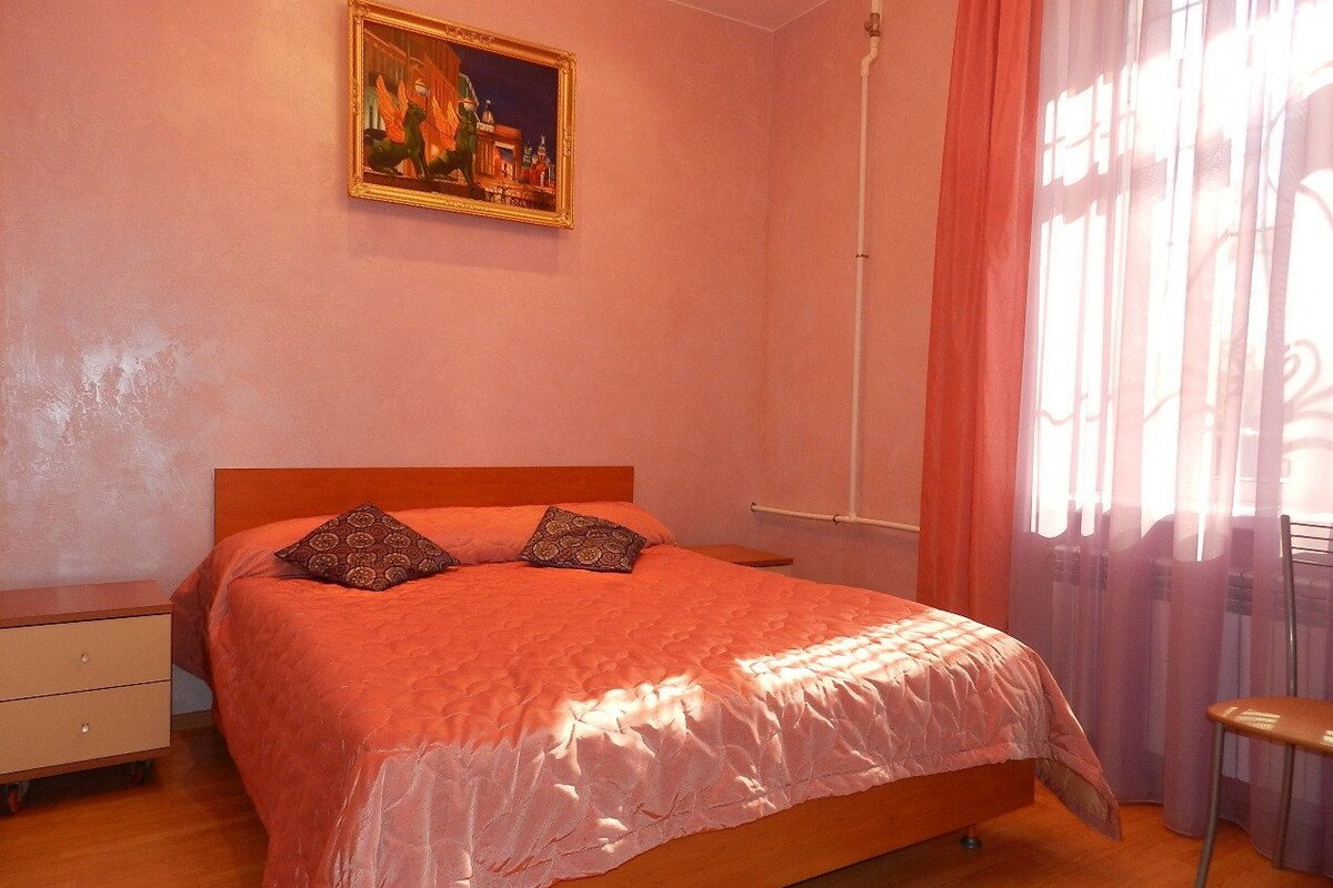 A bedroom with a bed, a nightstand, a chair, and a painting on the wall.