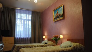 A hotel room with two beds, a painting on the wall, a window with curtains, and a desk with a lamp. - Guest House na Slobodskoy (St. Petersburg)